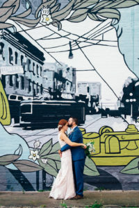 Downtown Tampa Creative Wedding Portrait, Bride in Sweetheart Lace Stella York Dress with White and Greenery Bouquet, Groom in Blue Suit