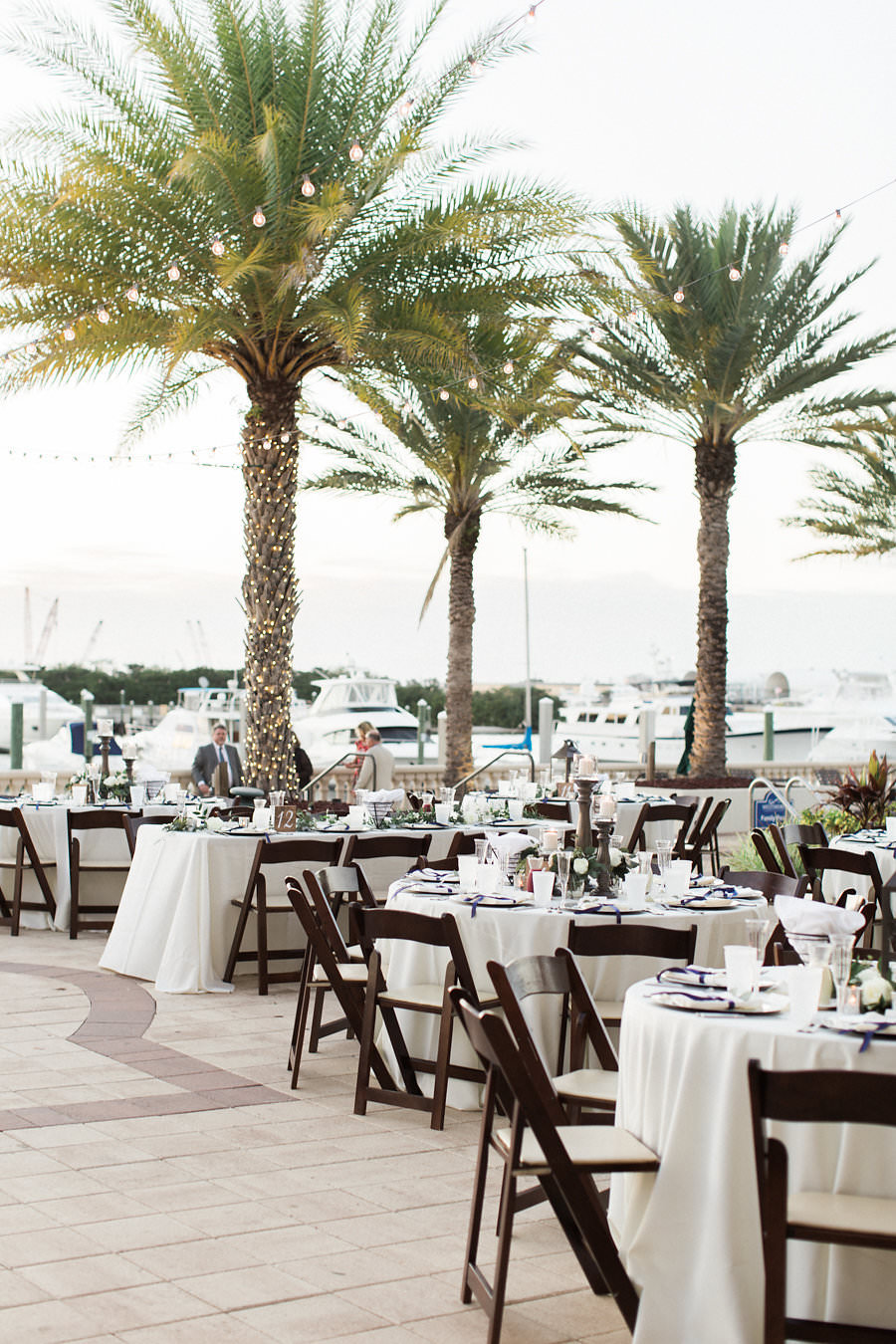 Outdoor Waterfront Wedding Reception with Round White Linen Tables, Blue Napkins, Wooden Folding Chairs | Tampa Bay Wedding Planner Unique Weddings and Events | Venue The Westshore Yacht Club