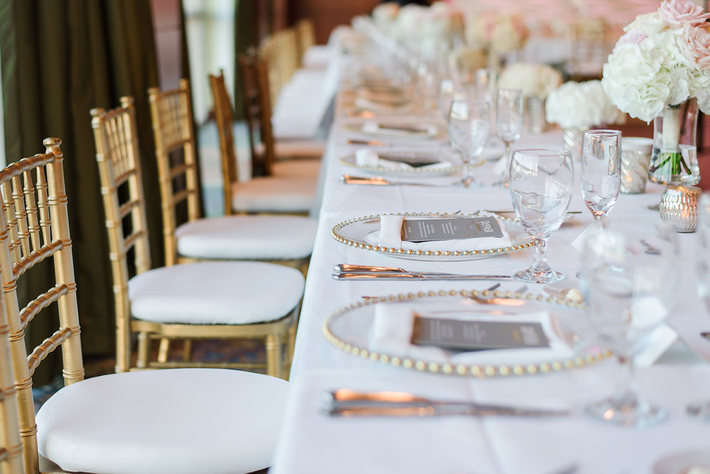 White and Gold Wedding Reception Feasting Table with Gray Printed Menus, Chiavari Chairs, Glass and Gold Beaded Chargers, and Small White and Pink Rose Centerpiece