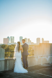 Industrial Chic Rooftop Wedding Portrait with Tampa Skyline, Bride in Mermaid Enzoani Dress, Groom in Blue Suit with Brown Shoes | Tampa Wedding Photographer Kera Photography