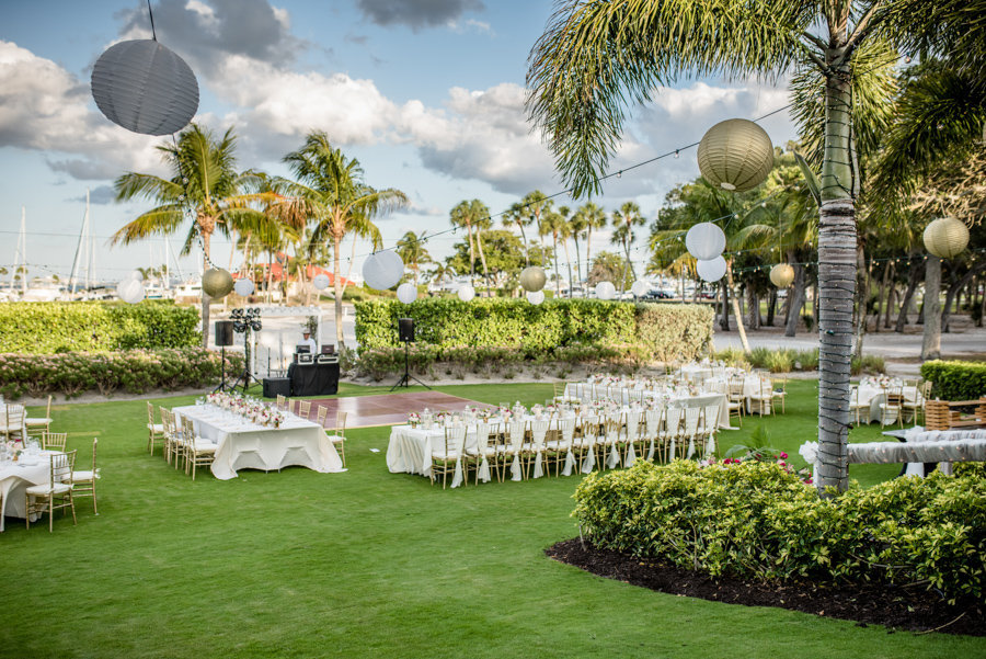 Outdoor Garden Wedding Reception with Long Feasting Tables with White Linen and Gold Chiavari Chairs, Palm Trees Wrapped in String Lights with White and Gold Chinese Paper Lanterns | Sarasota Wedding Planner NK Productions | Venue Lonboat Key Club