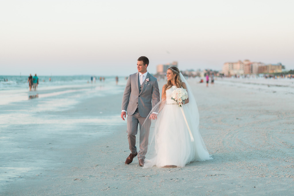 Outdoor Beach Wedding Bride and Groom Portrait, Groom in Gray Suit with Blush PInk Tie and Rose Boutonniere, Bride in Halter Ballgown Hayley Paige Wedding Dress with White Rose Bouquet and Jeweled Headband | Whimsical Clearwater Beach Wedding