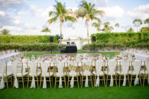 Outdoor Garden Wedding Reception with Long Feasting Tables with White Linens, Draped Gold Chiavari Chairs, Small Blush and Pink Centerpieces, Mr and Mrs Letters, Palm Trees Wrapped in String Lights with White and Gold Chinese Paper Lanterns | Sarasota Wedding Planner NK Productions | Venue Lonboat Key Club