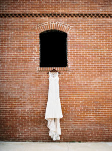Illusion Lace Neckline Column Stella York Wedding Dress on Hanger against Brick Wall