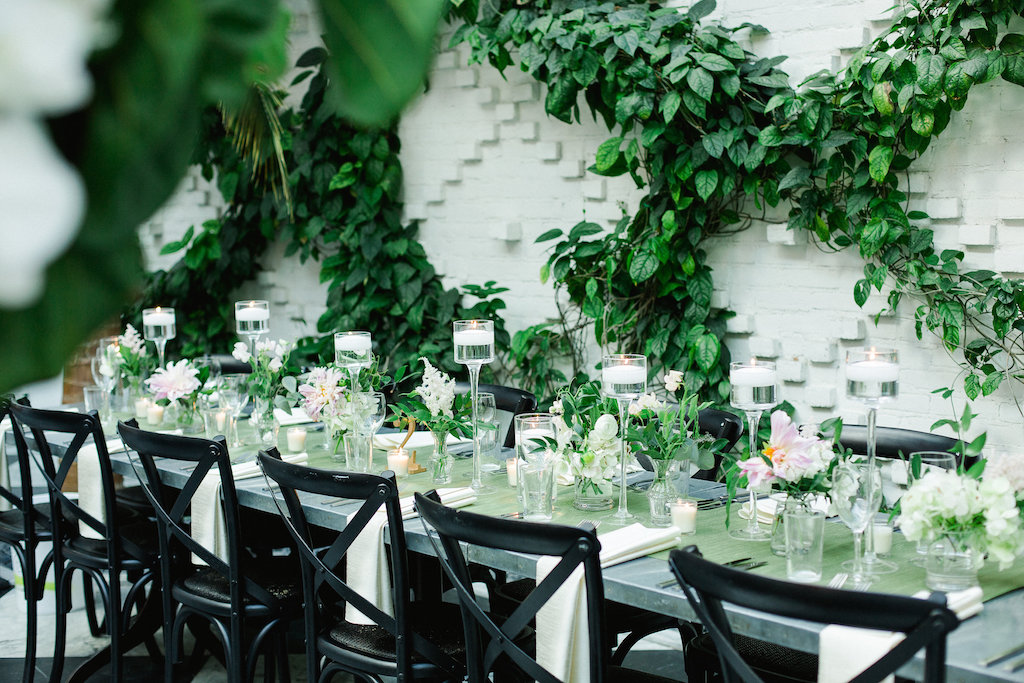 Indoor Ivory Garden Wedding Reception Industrial Metal Feasting Table with Low Pink and White Floral with Greenery Centerpieces, Black Crossback Chairs, and Floating Votive Candles in Tall Glass Holders | Downtown Tampa Wedding Venue The Oxford Exchange