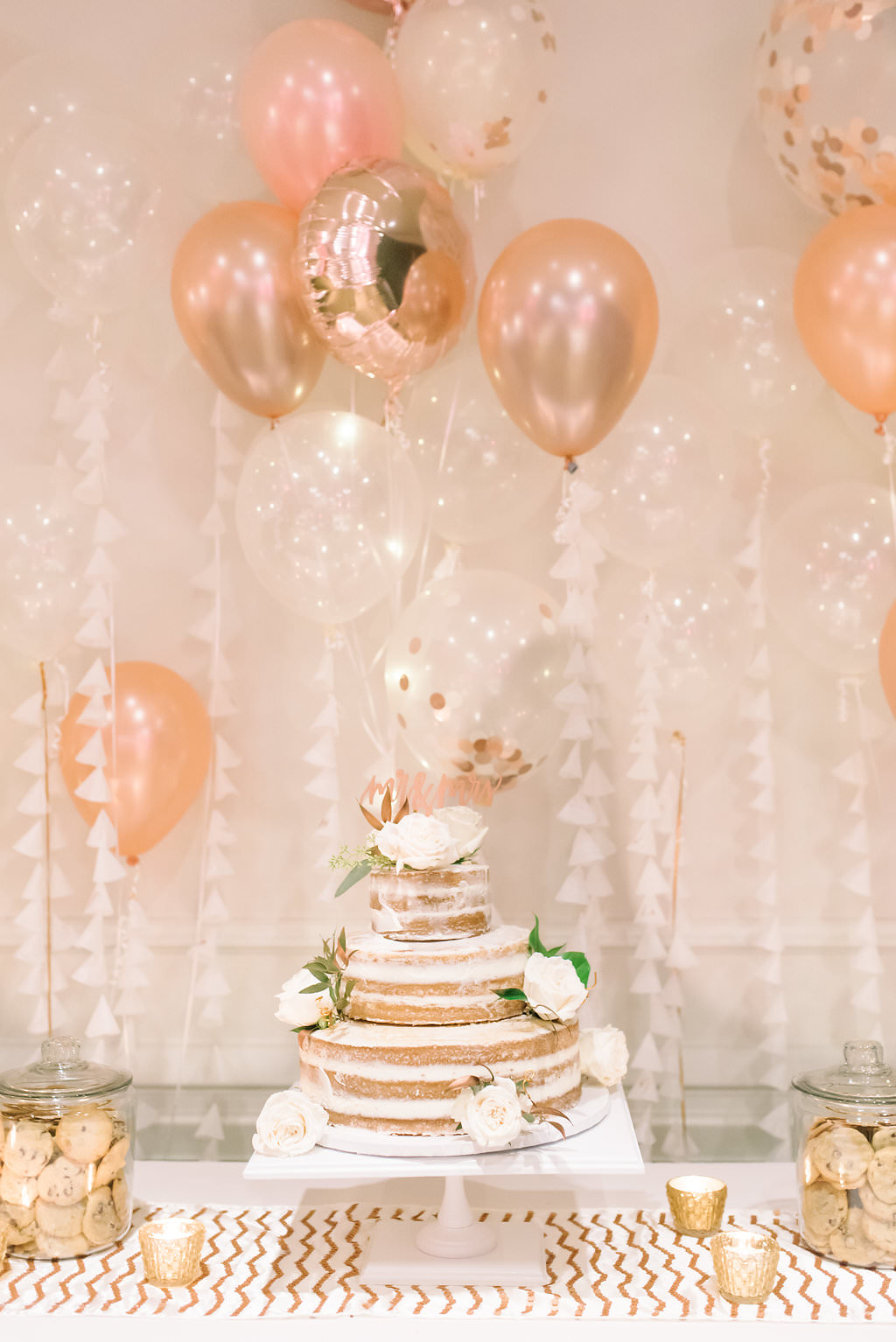 White and Copper Wedding Dessert Table with Three Tier Round Naked Frosting Cake with White ROses and Greenery, Chocolate Chip Cookies, and Rose Gold and Pink Balloons
