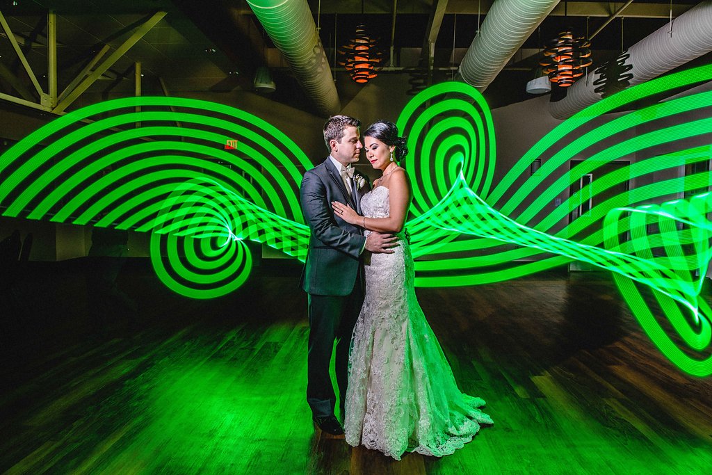 Creative Industrial Indoor Bride and Groom Portrait, Bride in Lace Column Strapless Dress, Groom in Gray Tuxedo, with Neon Green Light Art | Downtown St. Pete Wedding Venue NOVA 535