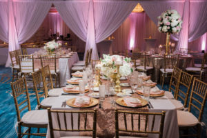 Whimsical Gold and Pink Hotel Ballroom Wedding Reception with Tall White Hydrangea Pink Rose and Greenery Centerpieces in Gold Vases, Gold Sequin Table Cloths, and Gold Chiavari Chairs and Stylish Gold Candlestick Holders and Table Numbers | Tampa Bay Wedding Draping, Linen, and Furniture Rental Gabro Event Services | Venue Hilton Clearwater Beach