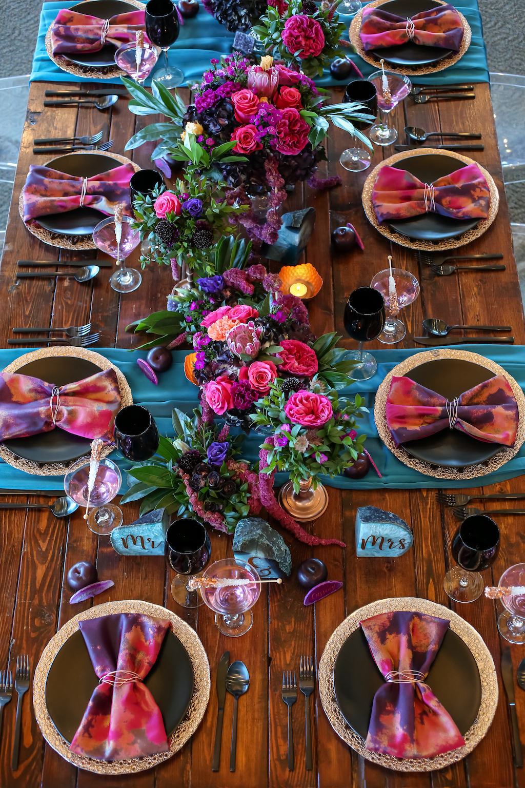 Vibrant, Modern Whimsical Wedding Reception Wooden Feasting Table with Black Flatware, Wine Glasses, and Plates, Copper Chargers and Votive Candleholders, Low Plum and Fuchsia Florals with Greenery Centerpieces, Pink and Purple Watercolor Napkins and Turquoise Linen Runners, Glitter Rock Candy Favors | Tampa Bay Wedding Planner Kelly Kennedy Weddings and Events | Furniture Rentals A Chair Affair | Florist Gabro Event Services