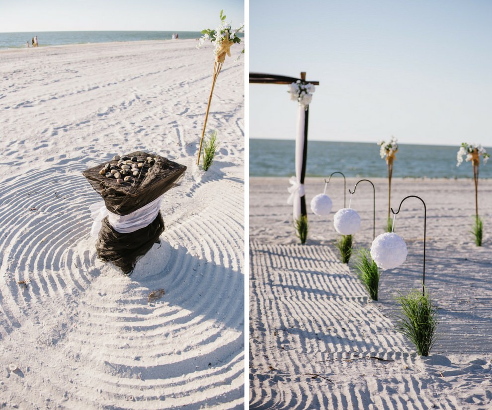 Simple Intimate Beach Wedding Ceremony Decor with White Pomander Balls on Iron Hook with Greenery, Black Tulle Draped Table, Wooden Arch with White FLowers and Draping, and Tiki Torches | Tampa Bay Wedding Planner Gulf Beach Weddings | Treasure Island Venue Sunset Vista Condo Hotel Resort 