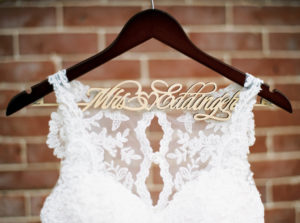 Illusion Lace Neckline Column Stella York Wedding Dress on Custom Gold and Wood Hanger against Brick Wall