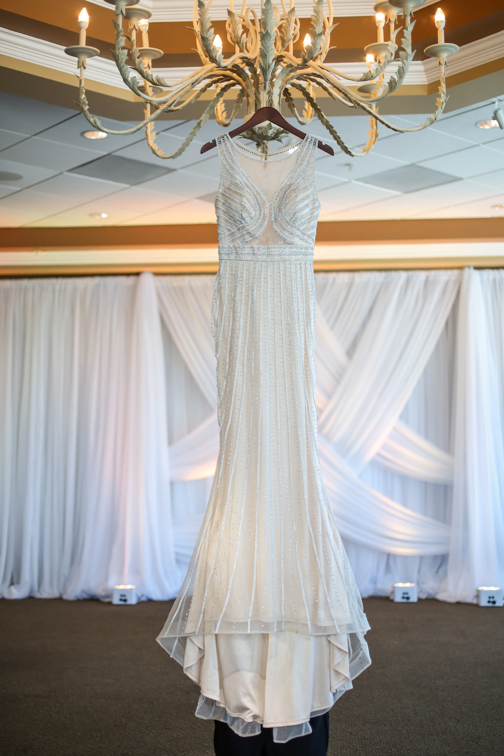 Jeweled Illusion V Neck Wedding Dress on Hanger with Chandelier and White Draping | Tampa Bay Bridal Boutique Truly Forever Bridal | Wedding Rentals and Draping Gabro Event Services