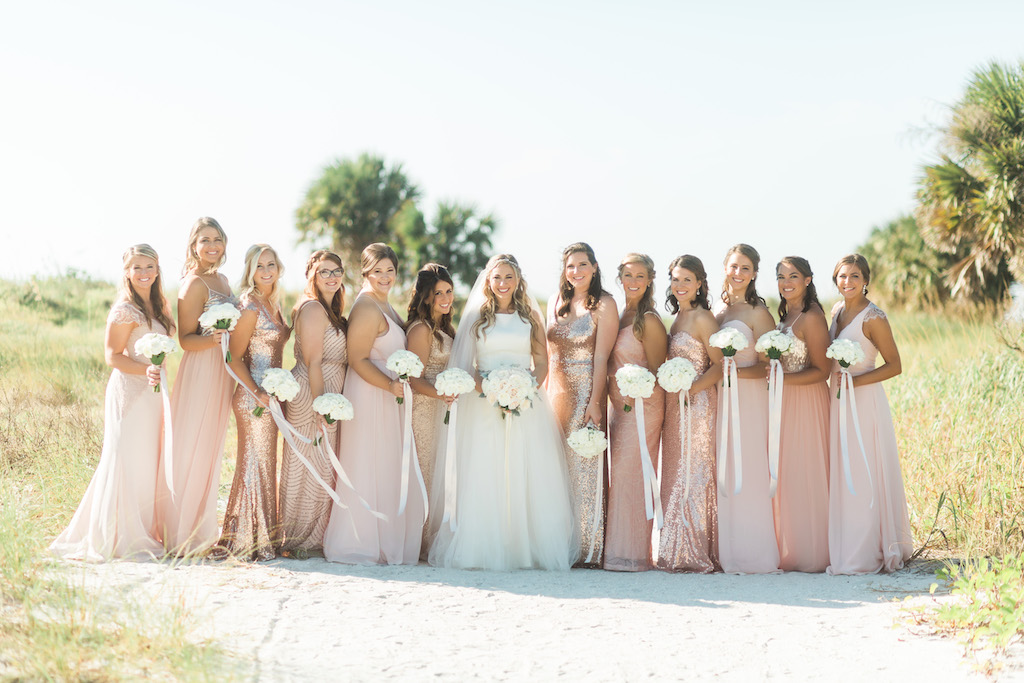 Outdoor Beachfront Bridal Party Portrait in Mismatched Pink, Blush, Rose Gold Sequin Mismatched Bella Bridesmaids Dresses, Bride in Halter Ballgown Hayley Paige Dress, with White Floral Bouquets with Long Ribbons | Clearwater Beach Wedding