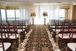 Indoor Hotel Wedding Ceremony Decor with White Hydrangea and Blush Pink Rose with Greenery Flowers in Glass Vases on Ornate Gold Pillars, and Floating Votive Candles on Gold Pedestals with Petal Aisle and Wooden Chiavari Chairs with White Cushions | Downtown Tampa Wedding Venue The Tampa Club