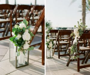Outdoor Waterfront Wedding Ceremony Decor Details with Pillar Candles in Hurricane Lanterns with White Garden Roses and Greenery, and Wooden Folding Chairs | Tampa Bay Wedding Planner Unique Weddings and Events | Venue The Westshore Yacht Club