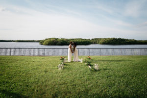 Outdoor Waterfront Wedding Portrait, Bride in Halter BHDLN Pantsuit and Beaded Strapless David's Bridal Dress, with Hurricane Lanterns, and Orange Flowers with Tropical Greenery | Tampa Waterfront Hotel Wedding Venue DoubleTree Suites by Hilton