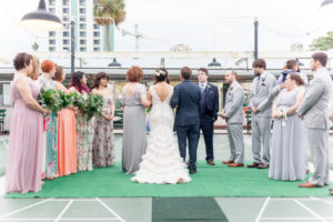Outdoor Wedding Ceremony Portrait, Bride in Open Backed A Line Fringe David's Bridal Dress, Groomsmen in Gray Suits, Groom in Navy Blue, Bridesmaids in Mismatched Pastel Floral Print Dresses with Greenery Bouquets | Unique Historic Downtown St Pete Wedding Venue St Petersburg Shuffleboard Club