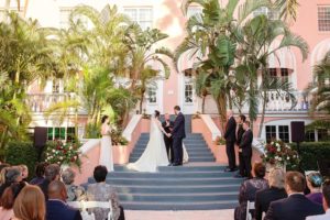 Outdoor Hotel Courtyard Wedding Ceremony Portrait with Red and White Rose Florals with Greenery | Historic Waterfront Hotel St. Pete Beach Wedding Venue The Don CeSar | Photographer Marc Edwards Photographs | Planner Parties A La Carte