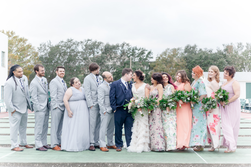 Outdoor Wedding Party Portrait, Bride in V Neck A Line Fringe David's Bridal Dress, Groomsmen in Gray Suits, Groom in Navy Blue, Bridesmaids in Mismatched Pastel Floral Print Dresses with Greenery Bouquets | Unique Historic Downtown St Pete Wedding Venue St Petersburg Shuffleboard Club
