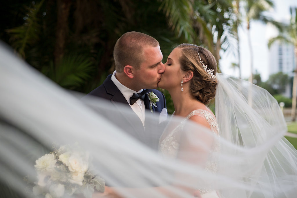 Outdoor Hotel Garden Wedding Portrait, Bride in Beaded Dress with White Rose and Greenery Bouquet and Silver Floral Hair Accessory, Groom in Navy Suit with White Floral Boutonniere and Black Bow Tie | Sarasota Wedding Photographer Cat Pennenga Photography