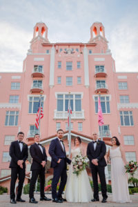 Outdoor Wedding Party Portrait, Groom in Navy Suit, Groomsmen in Black, Bridesmaid in Simple White Belted Column Dress, Bride with Pink Portea, Blush and White Floral with Greenery Bouquet in front of Historic St. Pete Beach Waterfront Hotel The Don CeSar | Photographer Marc Edwards Photographs