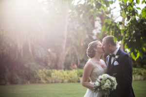 Outdoor Hotel Garden Wedding Portrait, Bride in Beaded Dress with White Rose and Greenery Bouquet and Silver Floral Hair Accessory, Groom in Navy Suit with White Floral Boutonniere and Black Bow Tie | Sarasota Wedding Photographer Cat Pennenga Photography