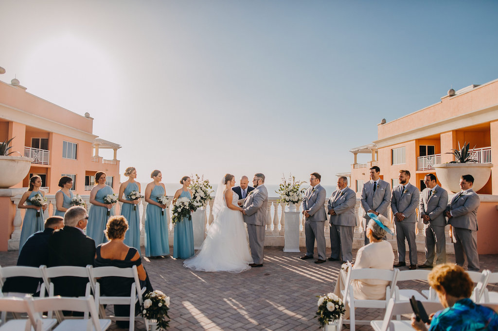 Waterfront Hotel Wedding Rooftop Ceremony Portrait, Bride in Ballgown Hayley Paige Dress, Groomsmen in Gray Suits with Black Ties, Bridesmaids in MIsmatched Light Blue Weddington Way Dresses, with White Folding Chairs, Ivory FLorals with Greenery in Hurricane Lanterns in Aisle and on Pedestals | Tampa Bay Wedding Venue Hyatt Regency Clearwater Beach and Spa | Photographer Rad Red Creative