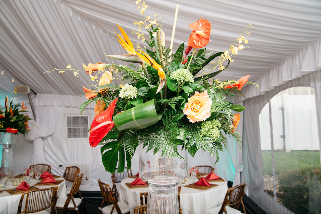 Tented Waterfront Wedding Reception with Tall Bird of Paradise Orange and Yellow Floral with Tropical Greenery Centerpiece in Glass Vase, with Guava Pink Napkins and Rattan Folding Chairs | Tampa Bay Wedding Venue DoubleTree Suites by Hilton