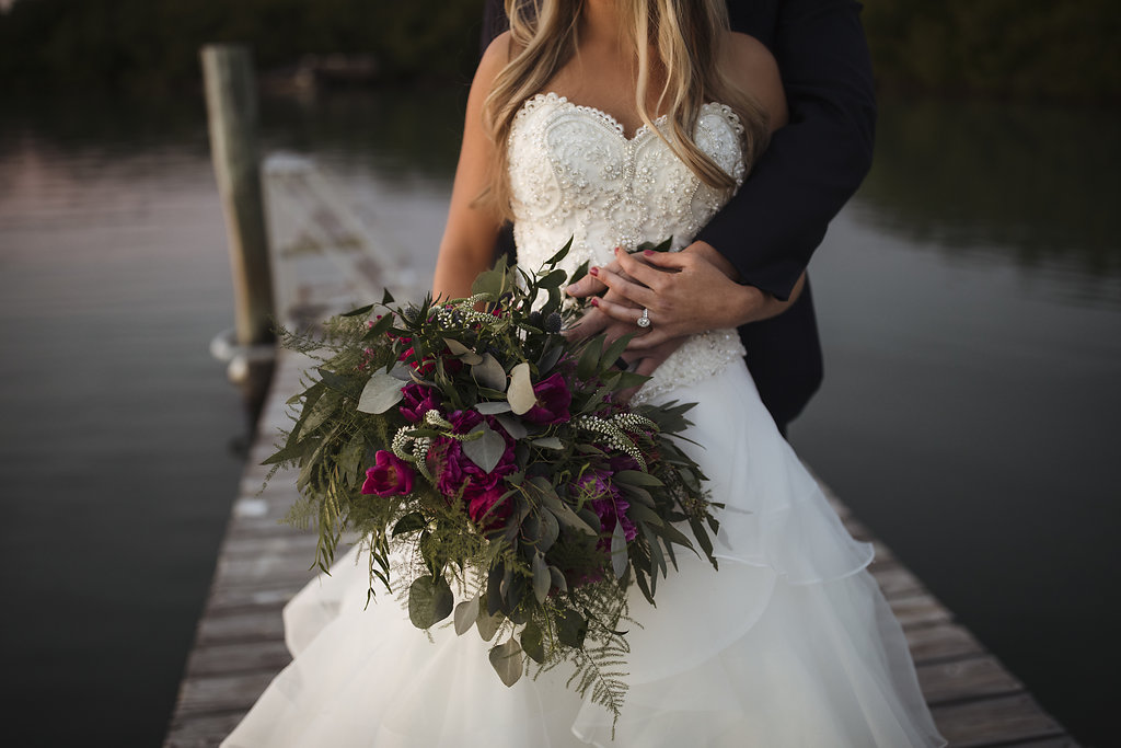 Outdoor Waterfront Dock Wedding Portrait, Bride in Strapless Beaded Layered Ballgown Dress with Fuchsia Floral and tropical Greenery Bouquet | Venue Longboat Island Chapel