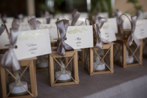 Elegant Mini Hurricane Lantern WEdding Favors on Table with Gold Foil Floral and Black Script Printed White Luggage Tag Escort Cards tied with Gray Ribbon