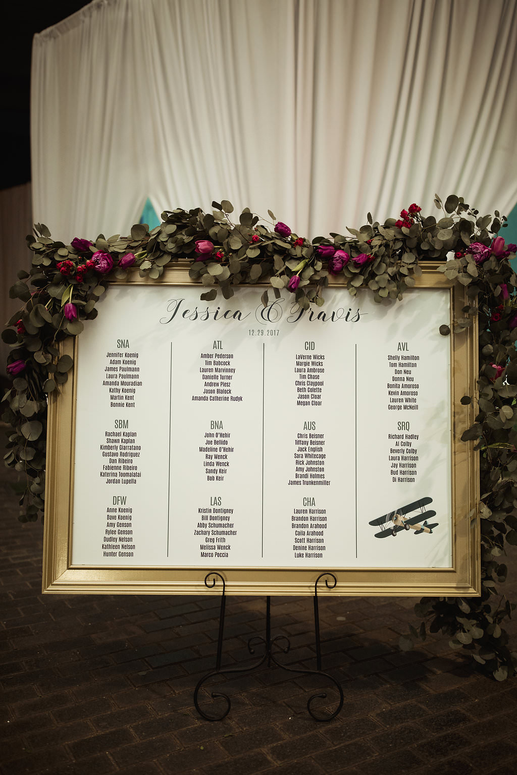 Jewel Toned Wedding Reception GOld Framed Black and White Printed Seating Chart with Airplane Illustration, Fuchsia and Greenery Garland and White Draping | Sarasota Wedding Planner Jennifer Matteo Event Planning
