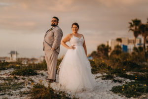 Outdoor Beach Sunset Wedding Portrait, Bride in Patterned Bodice Spaghetti Strap Ballgown Hayley Paige Dress, Groom in Gray Suit with BLack Tie and White with Greenery Boutonniere | Clearwater Beach Wedding Photographer Rad Red Creative | Bridal Hair and Makeup Femme Akoi Beauty Studio