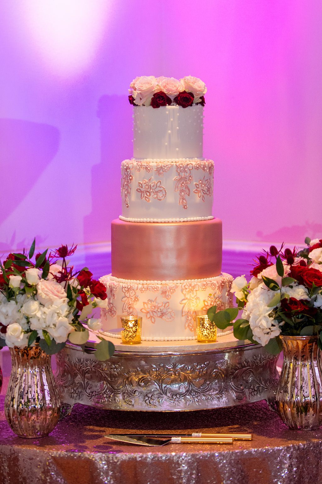 Four Tier Round White and Pink Wedding Cake with Rose Cake Topper on Silver Cake Stand, with Sequin Linen and Blush PInk, Burgundy, Red and Greenery Florals in Silver Vases