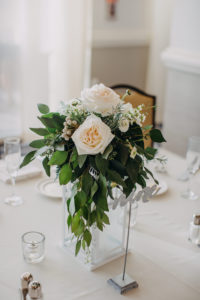 Indoor Hotel Ballroom Wedding Reception with Ivory Rose and White Floral with Natural Greenery Medium Height Centerpiece in Square White Hurricane Lantern, with Silver Glitter Table Number