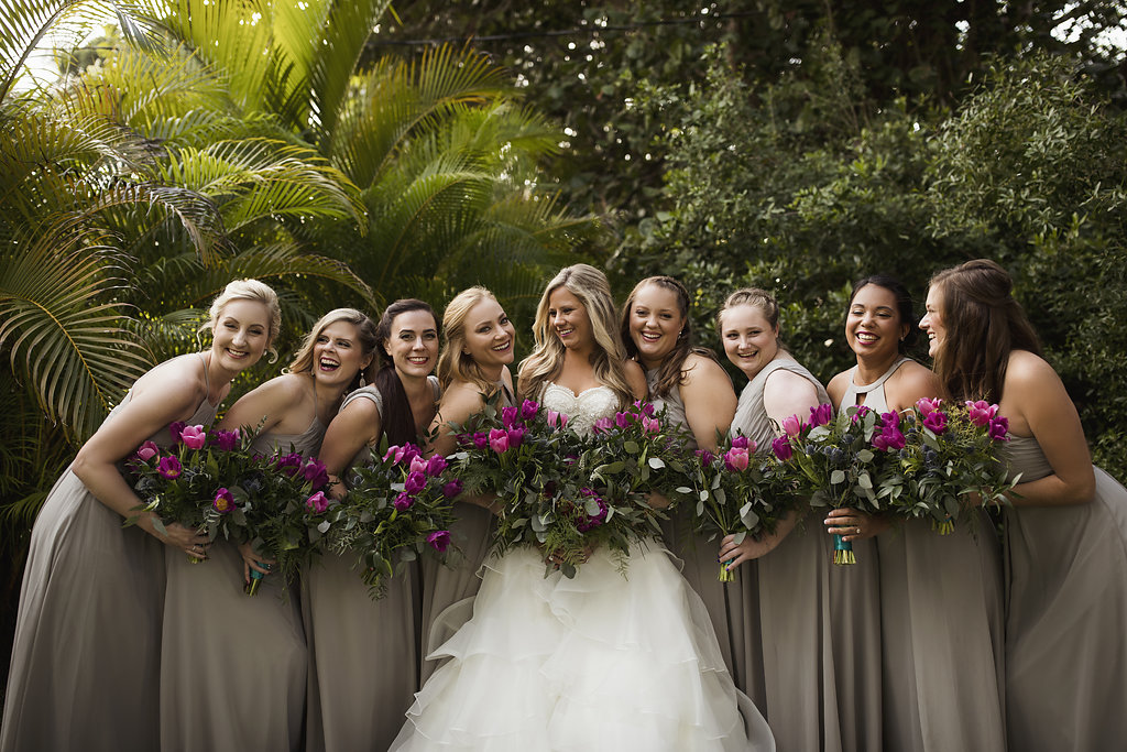 Outdoor Bridal Party Portrait In Strapless Layered Ballgown Wedding Dress with Fuchsia Floral and Greenery Bouquet Wrapped in Turquoise Ribbon, Bridesmaids in Mismatched Gray Azazie Dresses | Jewel Toned Longboat Key Wedding