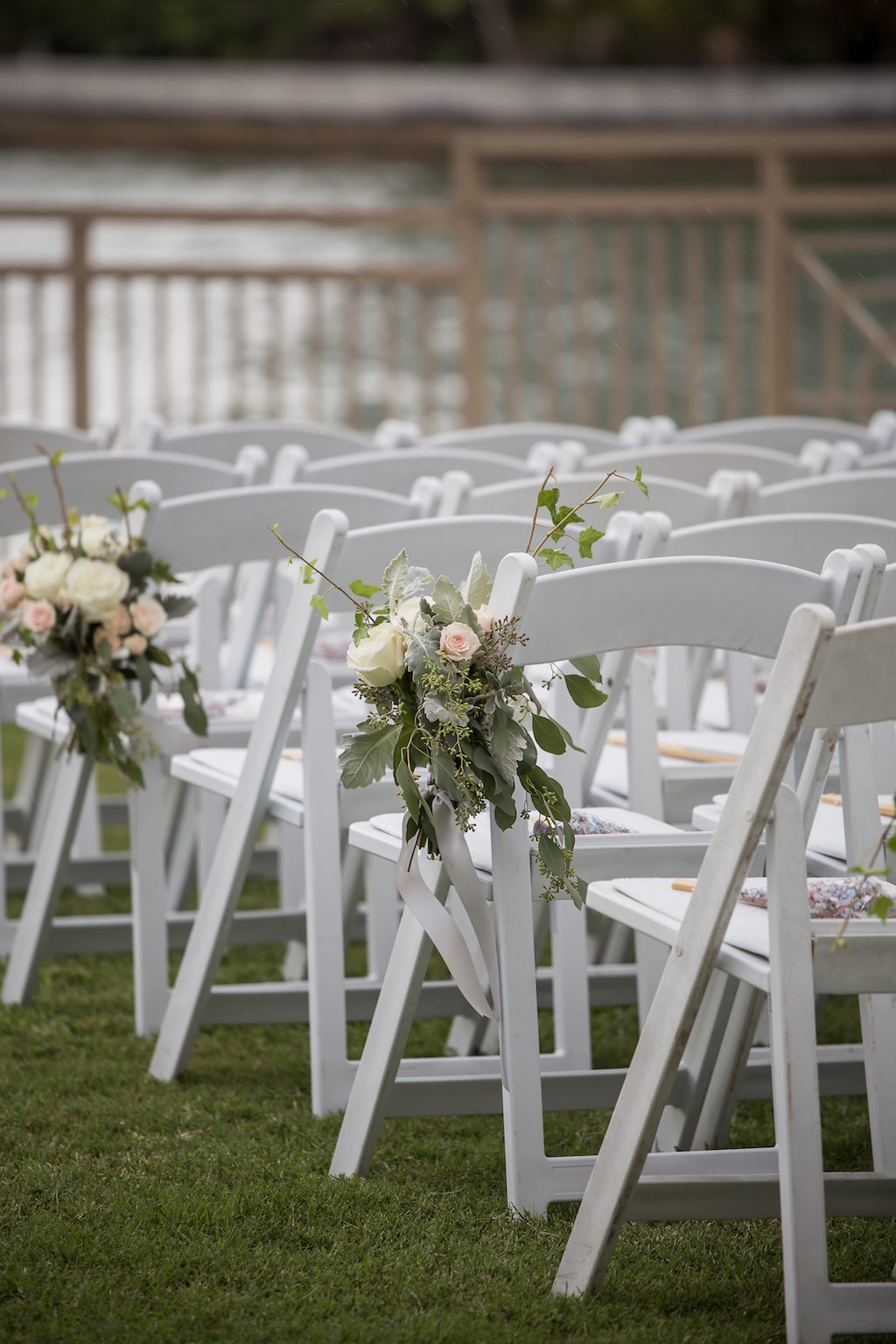 Outdoor Waterfront Garden Wedding Ceremony with Folding Chairs and White Rose, Peach Floral, and Greenery Flowers