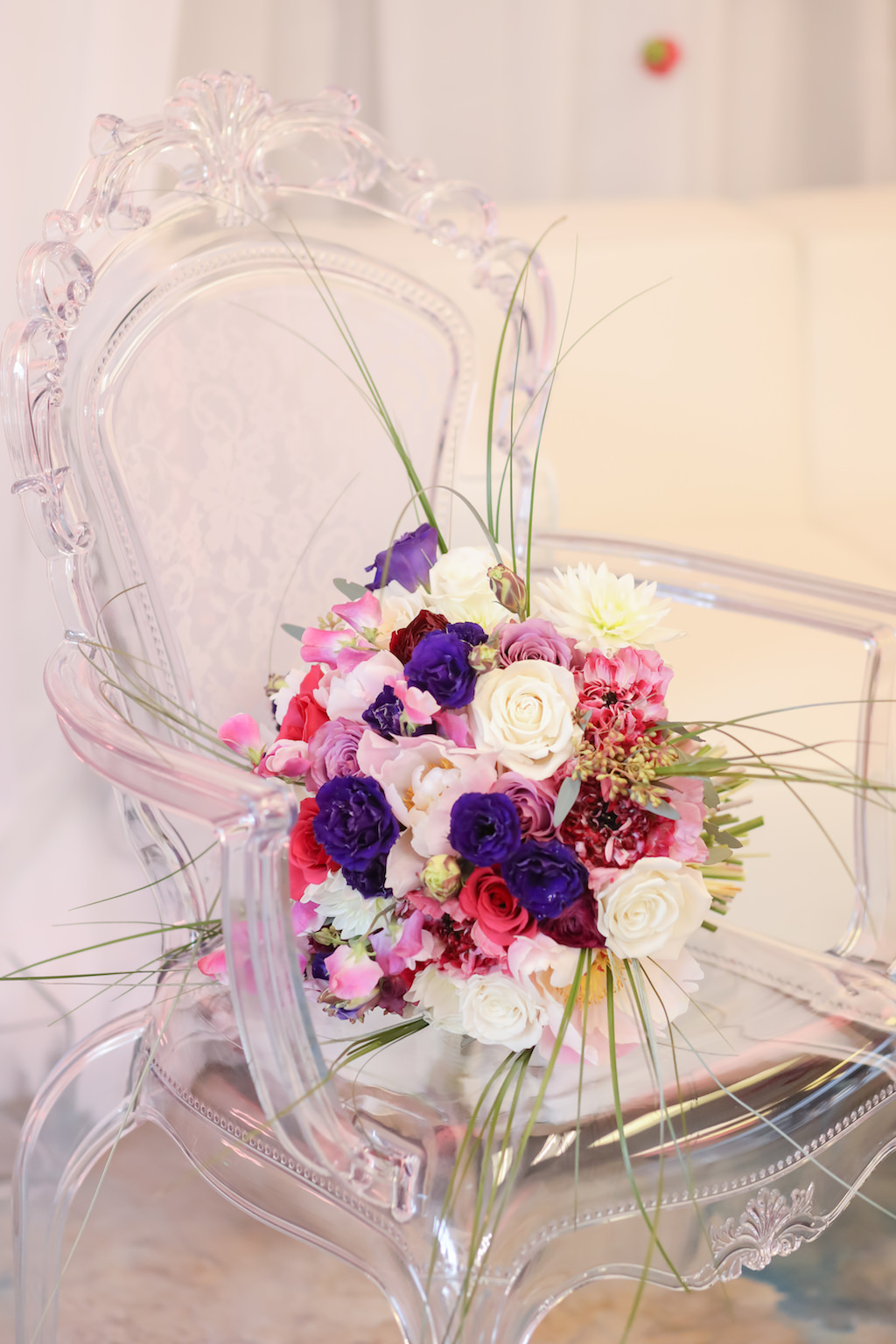Purple, White Rose, Pink and Red Floral with Decorative Grasses Bridal Bouquet in Victorian Inspired Clear Plastic Arm Chair | Clearwater FL Wedding Event Rentals and Florist Gabro Event Services