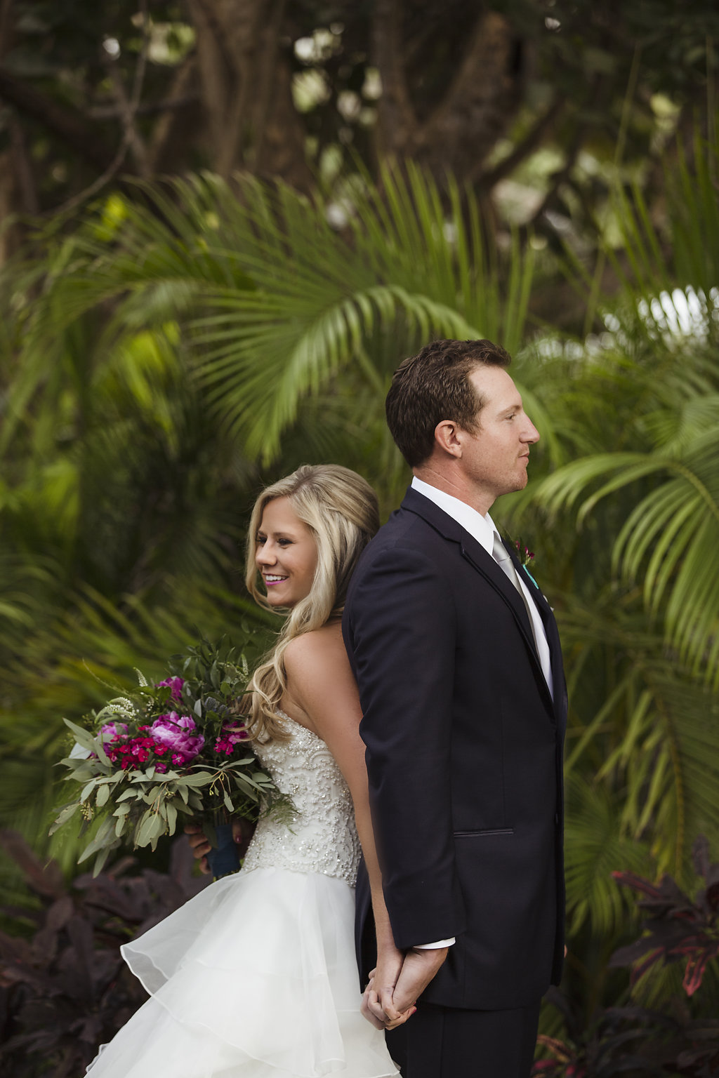 Outdoor Tropical Garden First Look Portrait, Bride In Strapless Layered Ballgown Wedding Dress with Fuchsia Floral and Greenery Bouquet Wrapped in Turquoise Ribbon | Jewel Toned Longboat Key Wedding