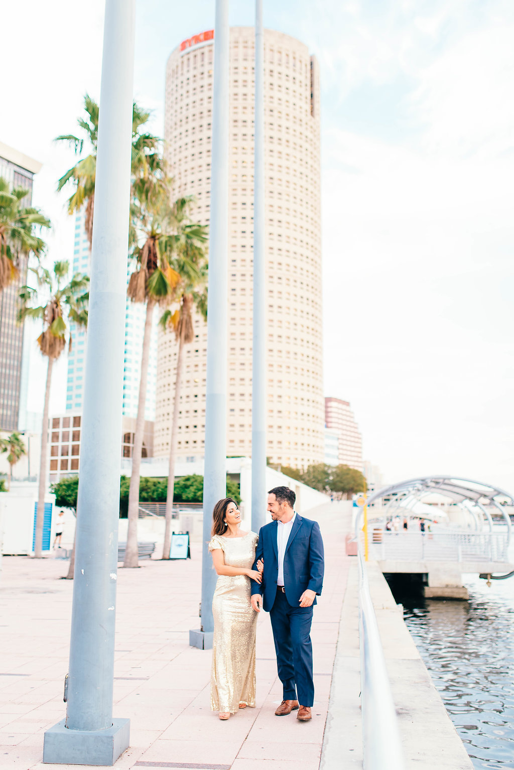 Downtown Tampa Riverwalk Classy Engagement Portrait, Bride in Long Gold Sequin Dress, Groom in Navy Blue Suit with Brown Leather Shoes