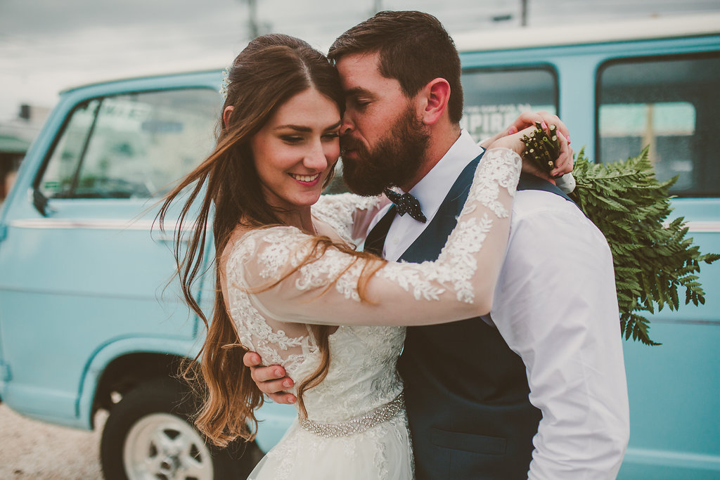 Outdoor Wedding Portrait, Bride in Lace Long Sleeve Belted Davids Bridal Wedding Dress with Green Fern and White Floral Bouquet, Groom in Navy Vest and Bow Tie | Downtown St Pete Outdoor Wedding Venue NOVA 535
