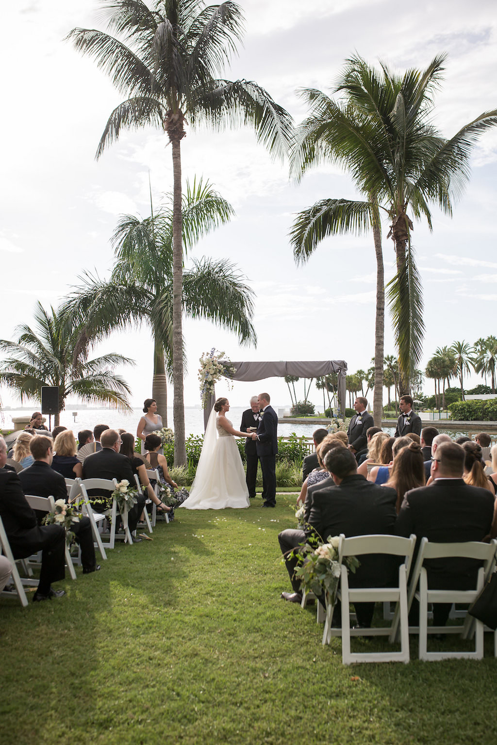 Outdoor Waterfront Downtown Hotel Wedding Ceremony Portrait with White Folding Chairs, Gray Silk Draped Ceremony Arch with White Florals | Sarasota Wedding Venue The Ritz Carlton | Tampa Bay Photographer Cat Pennenga Photography