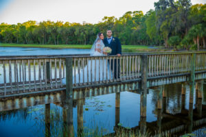 Outdoor Wedding Ceremony Portrait on Bridge, Bride in Ballgown Off the Shoulder Pronovias Dress with Pink and White Floral Bouquet, Groom in Black Suit with Blue Shirt and Boutonniere| Wedding Venue Tampa Palms Golf and Country Club