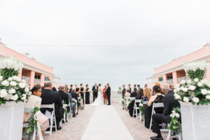 Waterfront Hotel Rooftop Elegant Wedding Ceremony Portrait with White Folding Chairs, White Rose and Greenery Floral Arrangements, and Fabric Aisle | Venue Hyatt Regency Clearwater Beach | Tampa Bay Wedding Planner Special Moments Event Planning | Florist Apple Blossoms Floral Designs | Photographer Kera Photography