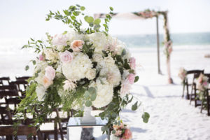 Siesta Beach Wedding Ceremony Decor with Wood Folding Chairs, Peach, BLush, and White Rose with Natural Greenery Florals on Mirrored Pedestal, and Ceremony Arch