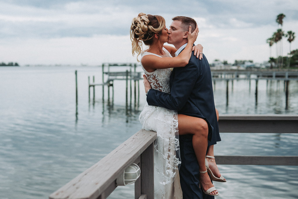 Outdoor Waterfront Wedding Portrait, Groom in Blue Suit with White Rose Boutonniere, Bride in Cutout V Neck Lace Dress | Tampa Bay Wedding Photographer Grind and Press Photography | Dunedin Venue Beso Del Sol