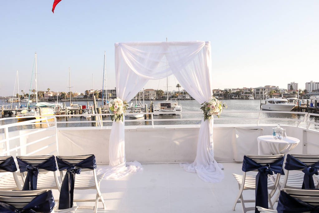 Outdoor Waterfront Wedding Ceremony Arch with White Draping, Blush Pink and White Rose with Greenery Florals, Folding Silver Chairs with Navy Blue Draping | Clearwater Beach Unique Wedding Venue Yacht Starship