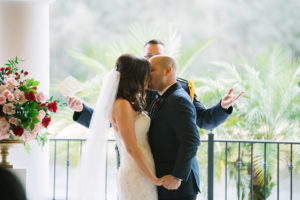 Outdoor Wedding Ceremony Portrait with Pink, Ivory, and Red Rose Florals with Greenery, Groom in Navy Suit with Wine Rose Boutonniere | Venue Tampa Palms Golf and Country Club | Event Planner Parties A La Carte