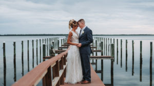 Outdoor Waterfront Wedding Portrait, Groom in Blue Suit with White Rose Boutonniere, Bride in Cutout V Neck Lace Dress | Tampa Bay Wedding Photographer Grind and Press Photography | Dunedin Venue Beso Del Sol