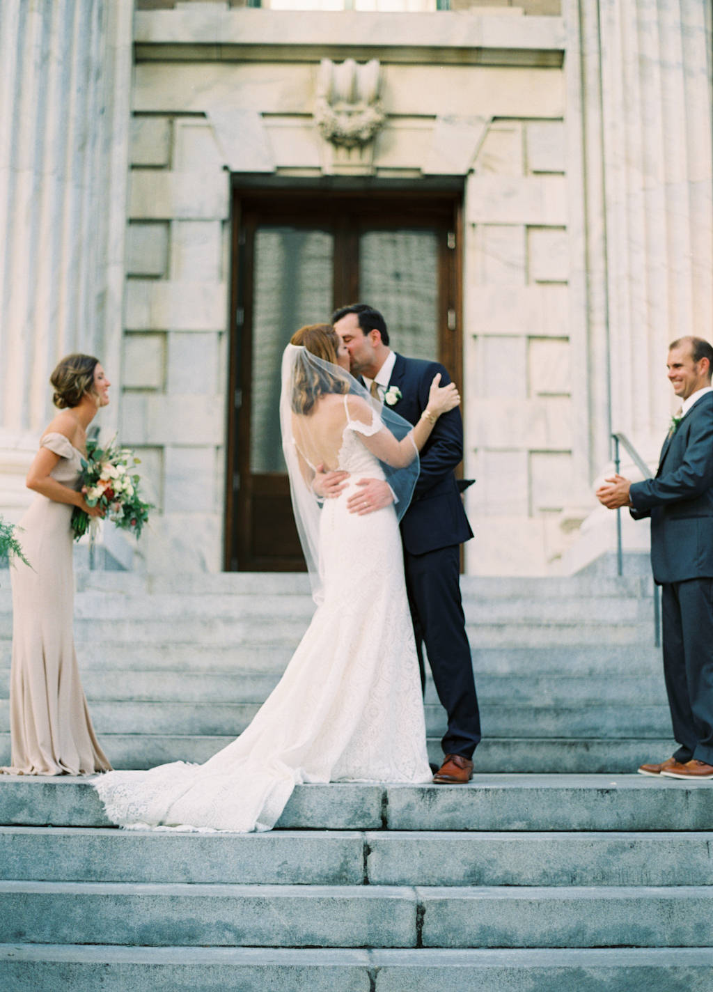 Outdoor Architectural Wedding Ceremony First Kiss Portrait on Front Steps of Downtown Tampa Hotel Venue Le Meridien Bridesmaid in Column Revolve Champagne Dress, Bride in Open Back Madeline Gardner Dress
