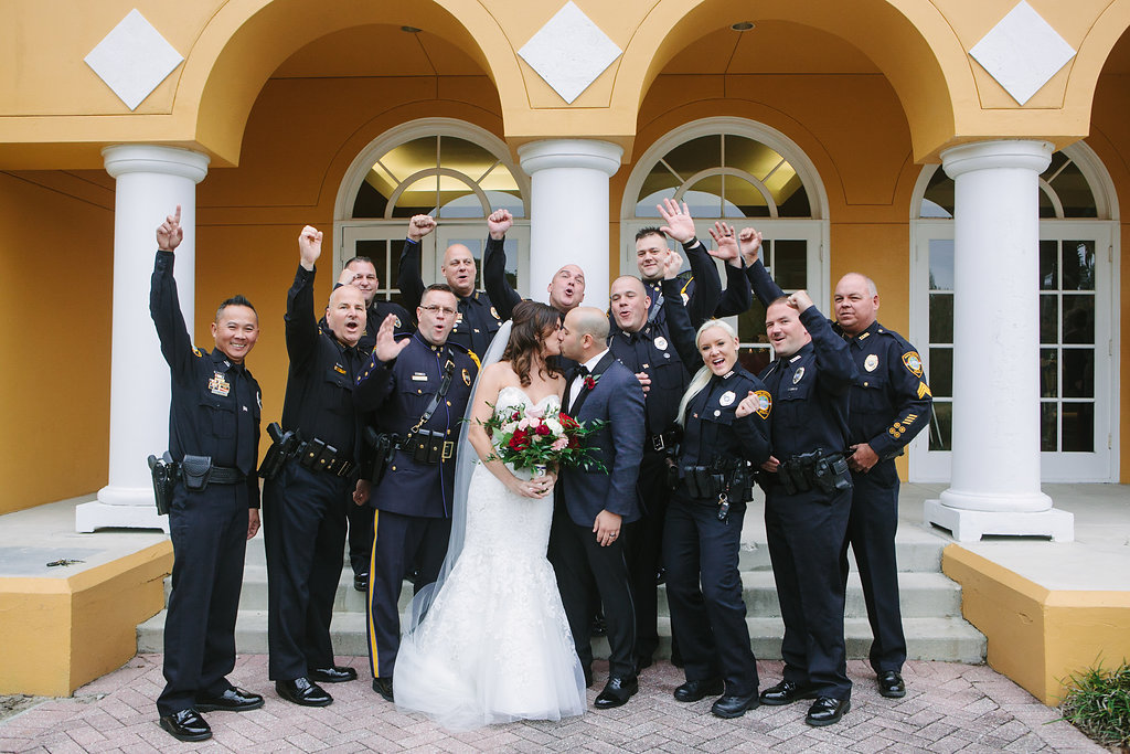 Outdoor Wedding Party Portrait with Pink, Ivory, and Red Rose Florals with Greenery, Groom in Navy Suit with Wine Rose Boutonniere, with Tarpon Springs Police Officers in Uniform | Venue Tampa Palms Golf and Country Club | Event Planner Parties A La Carte